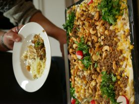 Eine Person hält einen Teller mit Schicht einem Gericht, daneben eine große Schale Salat mit FRoSTA-Tiefkühlprodukten und frischen Zutaten.