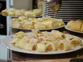 Nahaufnahme von Tellern mit FRoSTA-Tiefkühlprodukten wie gefüllten Crêpes, bestreut mit Nüssen oder Käse, im Hintergrund weiße Teller.