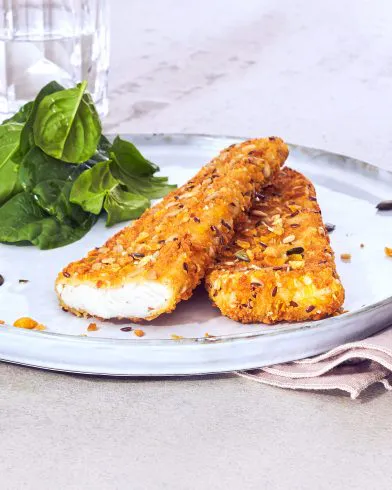 Ein Teller mit zwei FRoSTA Schlemmerfilet Fischfilets, eines davon so aufgeschnitten, dass das weiße Innere sichtbar ist, daneben frischer Spinat. Dahinter ein Glas Wasser.