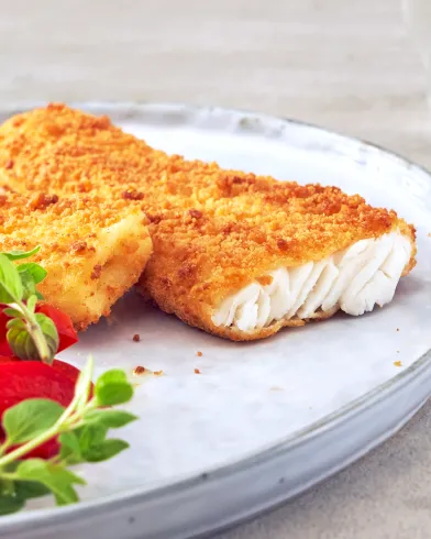 Zwei goldbraune Stücke FRoSTA Backofenfisch mit einer Prise Käse, garniert mit Kräutern und Tomaten. Der FRoSTA Fisch ist innen flockig und weiß.