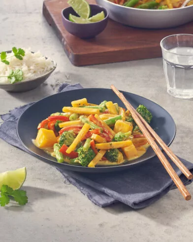 Ein Gericht aus FRoSTA Tiefkühl-Gemüsepfanne Curry mit Brokkoli, Paprika und Mango in Kokossauce, dazu Reis, Limette und Wasser.