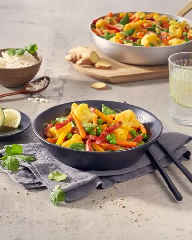 Eine schwarze Schüssel mit FRoSTA Tiefkühl-Gemüse – Karotten, Brokkoli, Erbsen & Paprika – steht auf einer grauen Serviette mit Stäbchen.