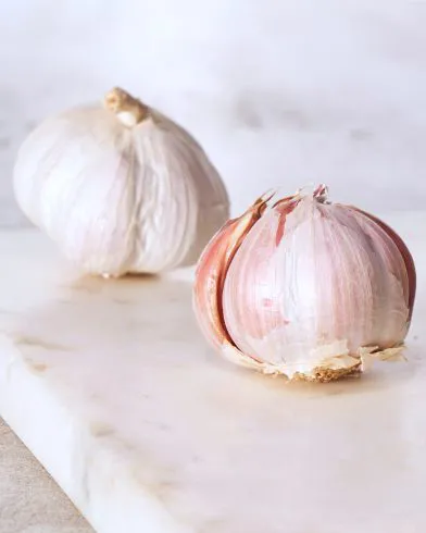 Zwei ganze Knoblauchknollen liegen auf einer hellen Marmorfläche – perfekt zu FRoSTA Tiefkühlprodukten im Hintergrund und Vordergrund.