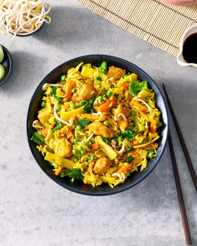 Eine Schüssel mit bunten FRoSTA Tiefkühlprodukten Nasi Goreng mit Tofu, Gemüse und Sprossen. Dazu Limette und extra Sprossen. Essstäbchen liegen daneben.