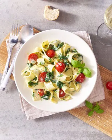 Ein Teller FRoSTA Pappardelle Crème Spinaci mit cremiger Sauce, Spinat, Kirschtomaten und frischem Basilikum, dazu Brot und Weißwein.