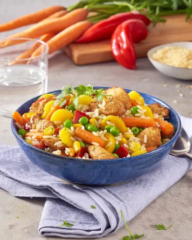 Eine lebendige FRoSTA Reispfanne mit Hähnchen, Reis, Gemüse & Kräutern liegt in einer blauen Schale auf einer Serviette im frischen Ambiente.