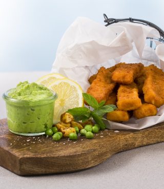 FRoSTA Fischstäbchen in einem Papierkörbchen mit veganem Erbsenpüree, Zitrone, Erbsen und Kräutern – ideal für Fans veganer Rezepte.