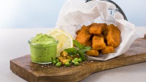 Goldbraune FRoSTA Tiefkühlprodukte-Fischstäbchen auf Holzbrett mit Erbsenpüree, Zitrone, Minze, Erbsen und Kartoffelwürfeln.