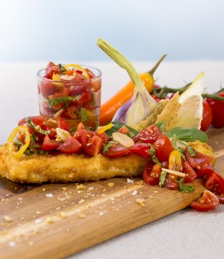 Ein FRoSTA Fischfilet in knuspriger Panade mit Tomaten-Basilikum-Salsa sowie Zitrone, Knoblauch, Karotten und frischem Basilikum.