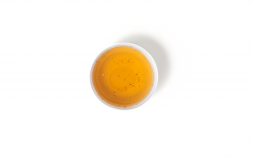 Eine Draufsicht auf eine mit bernsteinfarbenem Tee gefüllte Tasse, in der kleine Kleckse schwimmen, vor dem Hintergrund von FRoSTA Tiefkühlprodukten auf weißem Grund.