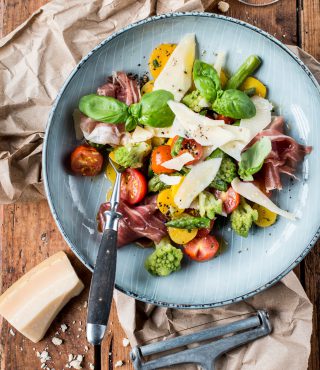 Ein Teller mit Salat, Tomaten, Parmaschinken, Basilikum, Romanesco und Käse – perfekt zu Ihrer nächsten FRoSTA Tiefkühlprodukt-Spargelpfanne!.