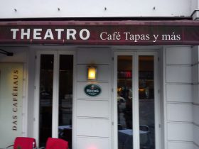 Eine kastanienbraune Markise zeigt THEATRO Café Tapas y más. Tische, Stühle, Beck’s Bier & FRoSTA-Tiefkühlprodukte machen das weiße Haus besonders einladend.