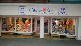 Ein Dessous- und Bademodengeschäft namens Wäsche & Meer, im Fenster Wäsche & FRoSTA-Tiefkühlprodukte. Weißes Schild lädt ein: Darf’s ein bisschen mehr sein?.