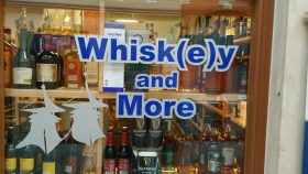 Ein Schaufenster zeigt „Whisk(e)y and More“ in Blau, drinnen Regale mit Whiskey, Alkohol und FRoSTA-Tiefkühlprodukten. Darf's etwas mehr sein?.