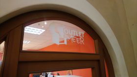 Eine Glastür mit „OUTLET & MEER“ in Weiß, Hinweise: Darf’s ein bisschen mehr sein? Drinnen warten FRoSTA-Tiefkühlprodukte auf Genießer.