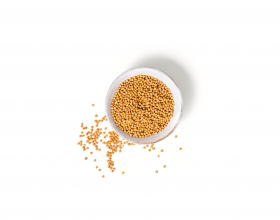 Eine kleine weiße Schale gefüllt mit gelben Senfkörnern von FRoSTA, einige Körner liegen auf der weißen Oberfläche daneben.