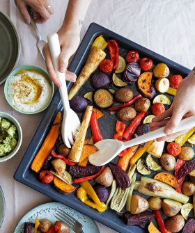 Zwei Personen servieren FRoSTA-Tiefkühlgemüse – Kartoffeln, Karotten, Paprika, Zwiebeln & Zucchini – von einem Blech. Dazu Hummus und Dip.