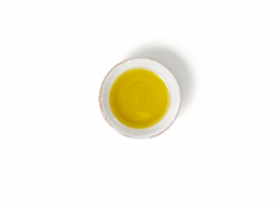 Eine kleine Keramikschale mit Sonnenblumenöl, daneben FRoSTA Tiefkühlprodukte, aus der Vogelperspektive auf weißem Hintergrund.