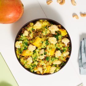 Auf einem weißen Tisch steht eine Schüssel gelbes Linsencurry mit FRoSTA Tiefkühlprodukten, Blumenkohl, Mango & Gemüse – inspiriert von Rezepturen aus aller Welt.