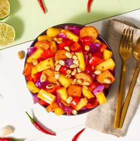 Ein bunter Obst-Gemüse-Salat mit FRoSTA-Tiefkühlprodukten, Erdnüssen, Chili, Limetten und goldfarbenem Besteck. Inspiration aus aller Welt!.