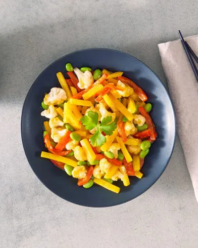 Eine dunkle Schale mit FRoSTA asiatische Gemüsepfanne, verfeinert mit Koriander. Stäbchen und Serviette liegen daneben.