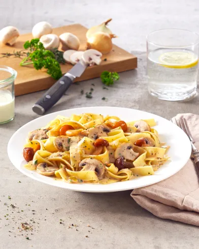 Bandnudeln mit Steinpilzen und Cherrytomaten in cremiger Sauce aus FRoSTA-Tiefkühlprodukten, dazu Wasser, frische Pilze und Kräuter.