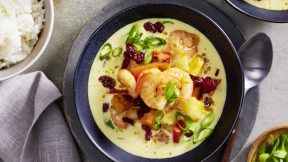 Ein Schälchen cremiges FRoSTA Garnelen Curry mit grünen Zwiebeln und Cranberries, serviert mit Reis. Öl, Löffel und Serviette daneben.