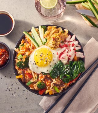 Eine Schüssel Bibimbap mit FRoSTA Tiefkühlprodukten: Reis, Gemüse, Kimchi, Spinat & Ei – ideal fürs OMR Festival. Dazu Sojasoße und Limettenwasser.