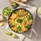 Eine Schüssel FRoSTA gebratener Gemüsereis, ideal für Gemüse Bowls-Fans: Brokkoli, Karotten & Edamame, serviert mit Limette und Ingwer.