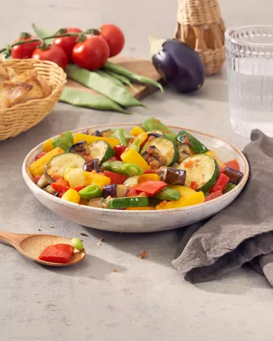 Eine Schale FRoSTA Gemüse Mix, mediterran inspiriert mit Zucchini, Auberginen, Paprika und grünen Bohnen. Dazu Brot, Tomaten und Wasser.