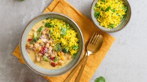 Eine Schüssel mit goldenem FRoSTA Kurkumareis und cremigem FRoSTA Kichererbsen Curry mit Kichererbsen, auf einer gelben Serviette mit Goldbesteck.