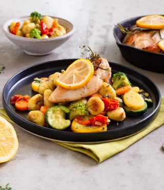 Ein Teller Zitronen-Ofen-Hähnchen mit FRoSTA Gnocchi-Pfanne, Zucchini, Brokkoli und Tomaten. Daneben FRoSTA Toscana-Gemüse.