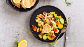 Ein schwarzer Teller mit gerösteter FRoSTA Gnocchi-Pfanne, Zucchini, Kirschtomaten, Karotten und Champignons, garniert mit Zitrone und frischen Kräutern.