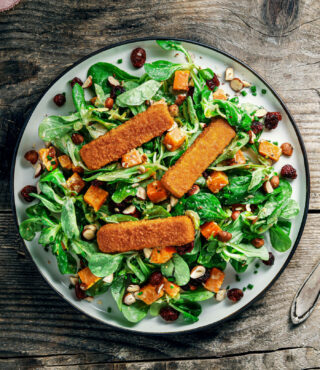 Ein Teller warmer Süßkartoffelsalat mit FRoSTA Veggie Fischstäbchen bietet Greens, Süßkartoffeln, Cranberries, Nüsse und drei knusprige Proteinstrips.
