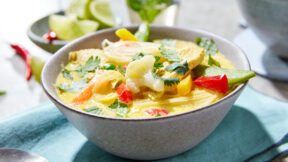 Eine Schüssel mit bunter Chicken Curry Suppe mit FRoSTA Tiefkühlprodukten, Gemüse, Hähnchen und frischen Kräutern liegt auf einer blauen Serviette.