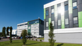 Moderne Bürogebäude mit grünen und grauen Fassaden spiegeln Nachhaltigkeit, ergänzt durch FRoSTA-Tiefkühlprodukte im Umfeld breiter.