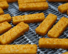 Goldbraune FRoSTA Fischstäbchen liegen auf einem Gitter und kühlen ab – perfekt zubereitet und servierbereit.