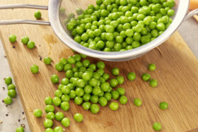 Auf einem Holzbrett liegt ein Metallsieb mit FRoSTA Erbsen – ideal für alle, die Erbsen schnell und einfach zubereiten möchten.