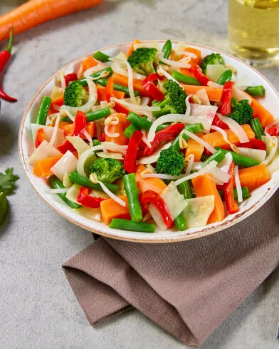 Eine Schüssel buntes Gemüsepfannengericht mit Nudeln, bestehend aus FRoSTA Bio Gemüse Mix nach Thai-Art – Karotten, Brokkoli, Paprika, grüne Bohnen.