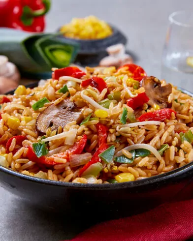 Eine Schüssel FRoSTA Bio Bratreis Asia Style Gemüse-Gebratener Reis mit Pilzen, Mais, Sojasprossen, Paprika und Kräutern.