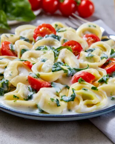 Ein Teller FRoSTA Tiefkühl-Bio Tortellini Crème Spinaci in cremiger Sauce mit Spinat und Tomaten, serviert auf blauem Teller.