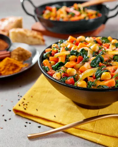 Eine Schüssel mit Gemüse-Kichererbseneintopf, inspiriert von FRoSTA Bio Gemüse Pfanne Orientalische Art, mit Karotten, Grünem und Sauce auf gelber Serviette.