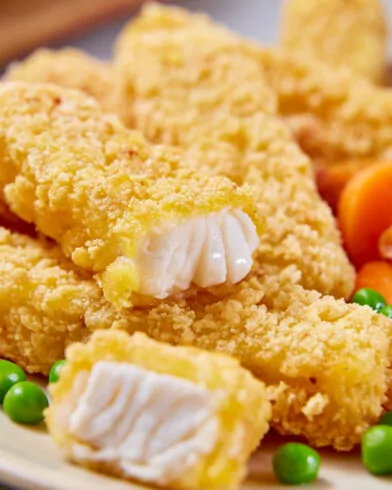 Nahaufnahme von knusprigen FRoSTA Cornflakes-Stäbchen auf einem Teller, dazu Erbsen, Karotten, Blumenkohl und goldene Kartoffelspalten.