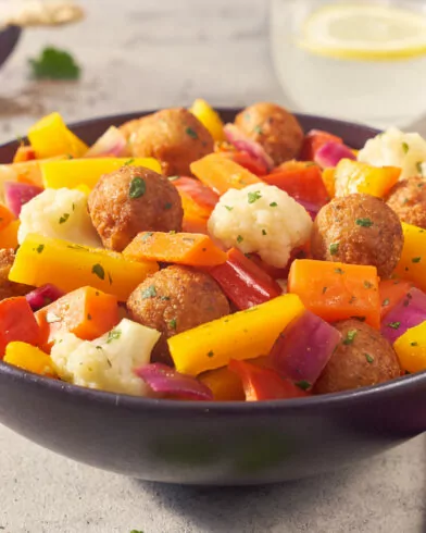 Eine bunte Falafel Bowl mit FRoSTA-Tiefkühlprodukten: geröstete Paprika, Karotten, Blumenkohl und roten Zwiebeln sowie Zitronenwasser.