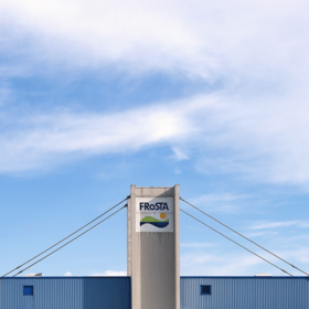 Ein hohes Gebäude mit blauem Dach und dem FRoSTA-Logo auf dem zentralen Turm steht vor einem hellen, bewölkten Himmel für Nachhaltigkeit.