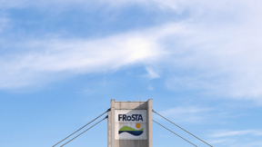 Ein hohes Gebäude mit blauem Dach und dem FRoSTA-Logo auf dem zentralen Turm steht vor einem hellen, bewölkten Himmel für Nachhaltigkeit.