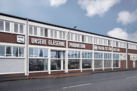 Eine große Ziegelei mit vielen Fenstern und deutschen Schildern wie „UNSERE GLÄSERNE PRODUKTION“ unterstreicht das Reinheitsversprechen von FRoSTA*Tiefkühlprodukte*.