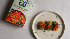 Eine Box FRoSTA Bio Gemüse Pfanne à la Mexicana liegt neben Polenta-Bites mit FRoSTA Mix – bunt, lecker und ideal für Snacks oder Partys.