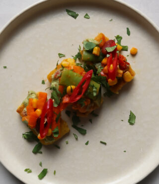 Ein beiger Teller mit zwei FRoSTA Polenta Bites, buntem Gemüse und frischem Koriander auf hellem Untergrund.