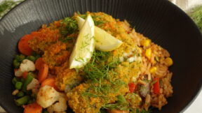 Eine schwarze Schüssel mit Reis, FRoSTA Tiefkühl-Gemüse, panierte Gemüsekoteletts wie Schlemmerfilet, frischem Dill und Zitrone – ein FRoSTA Bratreis-Genuss.